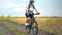A lady riding a VARUN M27-1 Electric bicycle on a dirt path with a clear sky