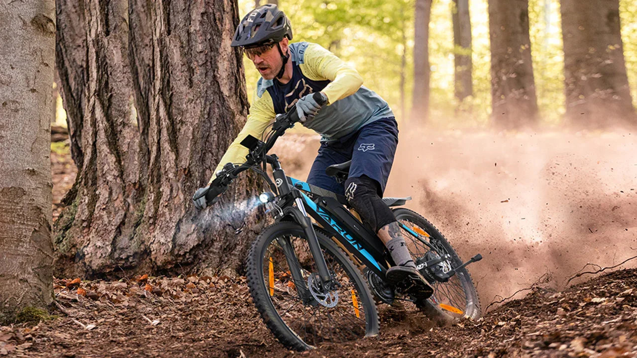 Person riding a VARUN M27-1 Electric mountain bike through a forest trail