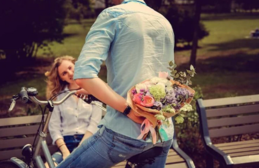 Electric bike lifestyle scene in park, man holding bouquet behind back, woman sitting on bench