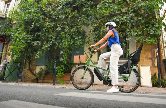 Woman riding a green electric cargo bike with rear seat on a city street side view