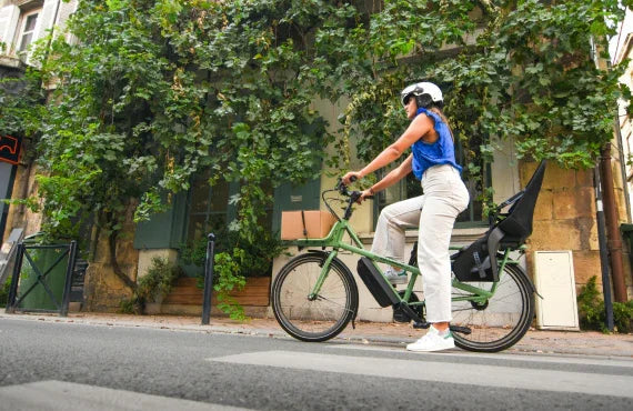 Woman riding green electric bike with cargo on city street, Pogo Cycles e-bike shop
