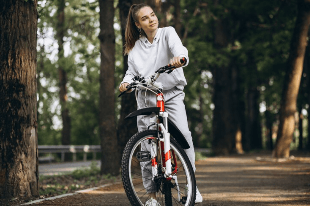 Woman in grey activewear with electric bike on forest path, Pogo Cycles e-bike for women