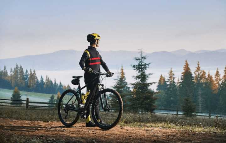 Electric mountain bike side view with rider on forest trail, wearing yellow helmet and gear