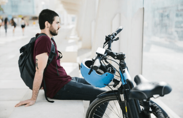 Man with backpack resting beside electric bike and helmet, e-bike store promo