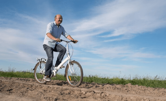 Senior man riding electric bike outdoors on dirt path, promoting Pogo Cycles e-bikes