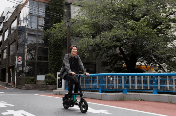 Electric bike ridden through urban street, black folding frame, side view, city background