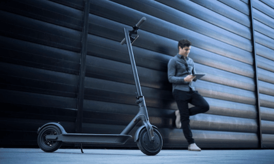 Electric scooter with man using tablet outside modern building at Pogo Cycles e bike store