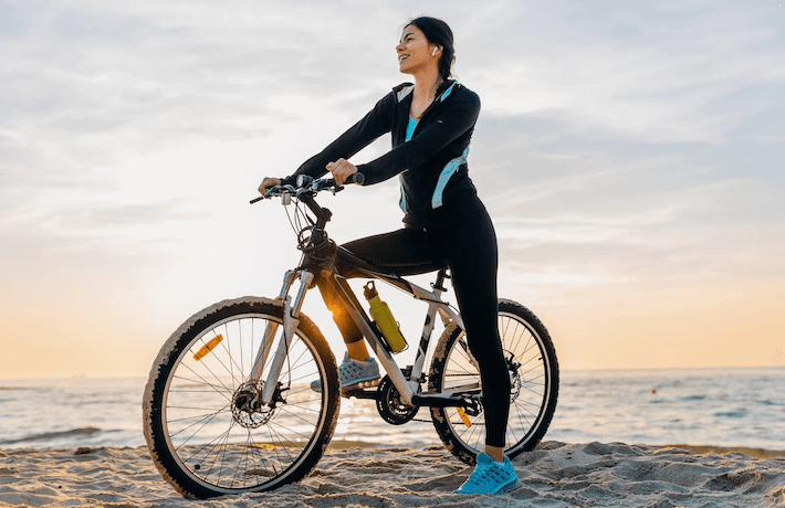 Electric bike with woman rider on a sandy beach at sunset, side view
