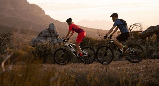 Two cyclists riding electric bikes on a scenic trail at sunset, Pogo Cycles adventure
